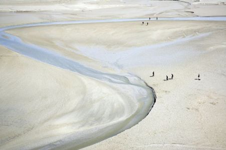 Endless pale beach, pale river twisting through, tiny human figures in two scant groups 