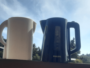 Two pitchers, one blue & one white, against a backdrop of green trees and open skies