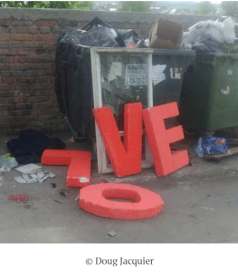 Overflowing dumpsters in front of a brick wall. Letter L-O-V-E toppled and discarded