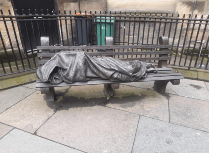 Brass sculpture of a homeless person, lying on a bench