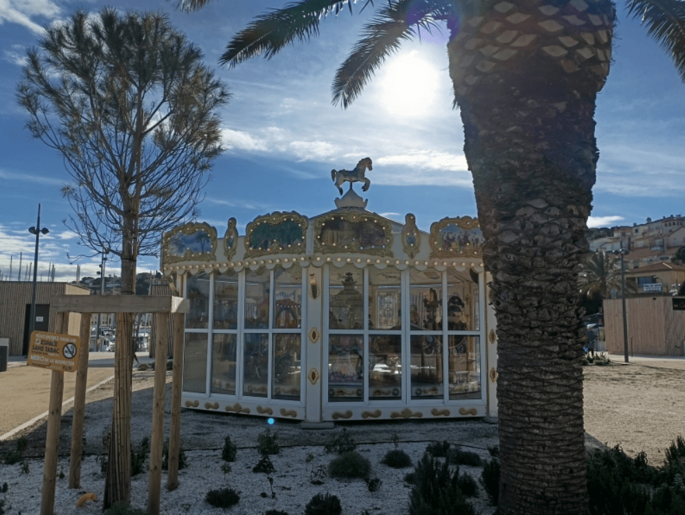 A glass-enclosed carousel on dry ground on a sunny late afternoon. Scene is deserted.